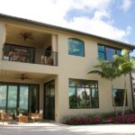A modern two-story home in Florida with a balcony, patio, and lush garden.
